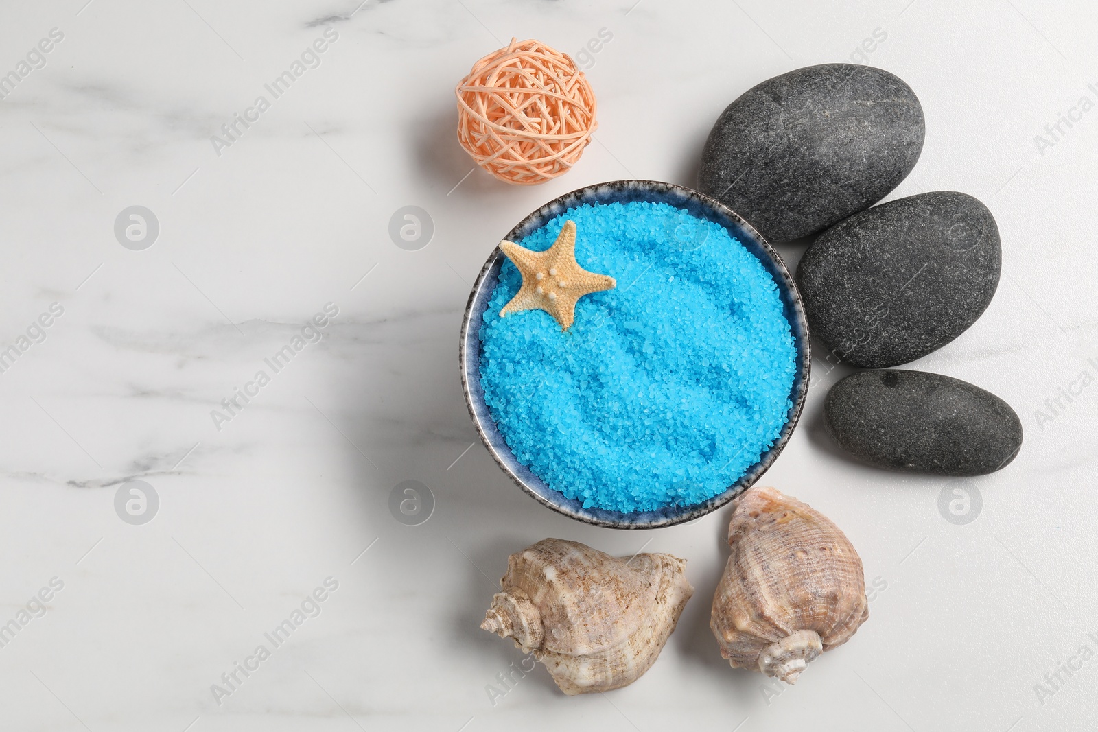 Photo of Light blue sea salt in bowl, spa stones, starfish and shells on white marble table, flat lay. Space for text