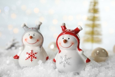 Photo of Christmas composition with decorative snowmen on artificial snow against blurred festive lights
