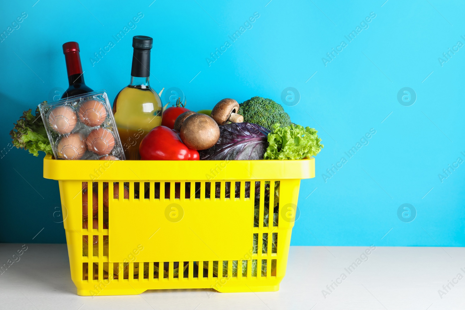 Photo of Shopping basket with grocery products on white table against light blue background. Space for text