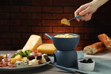 Photo of Woman dipping piece of potato into fondue pot with melted cheese at table with snacks, closeup