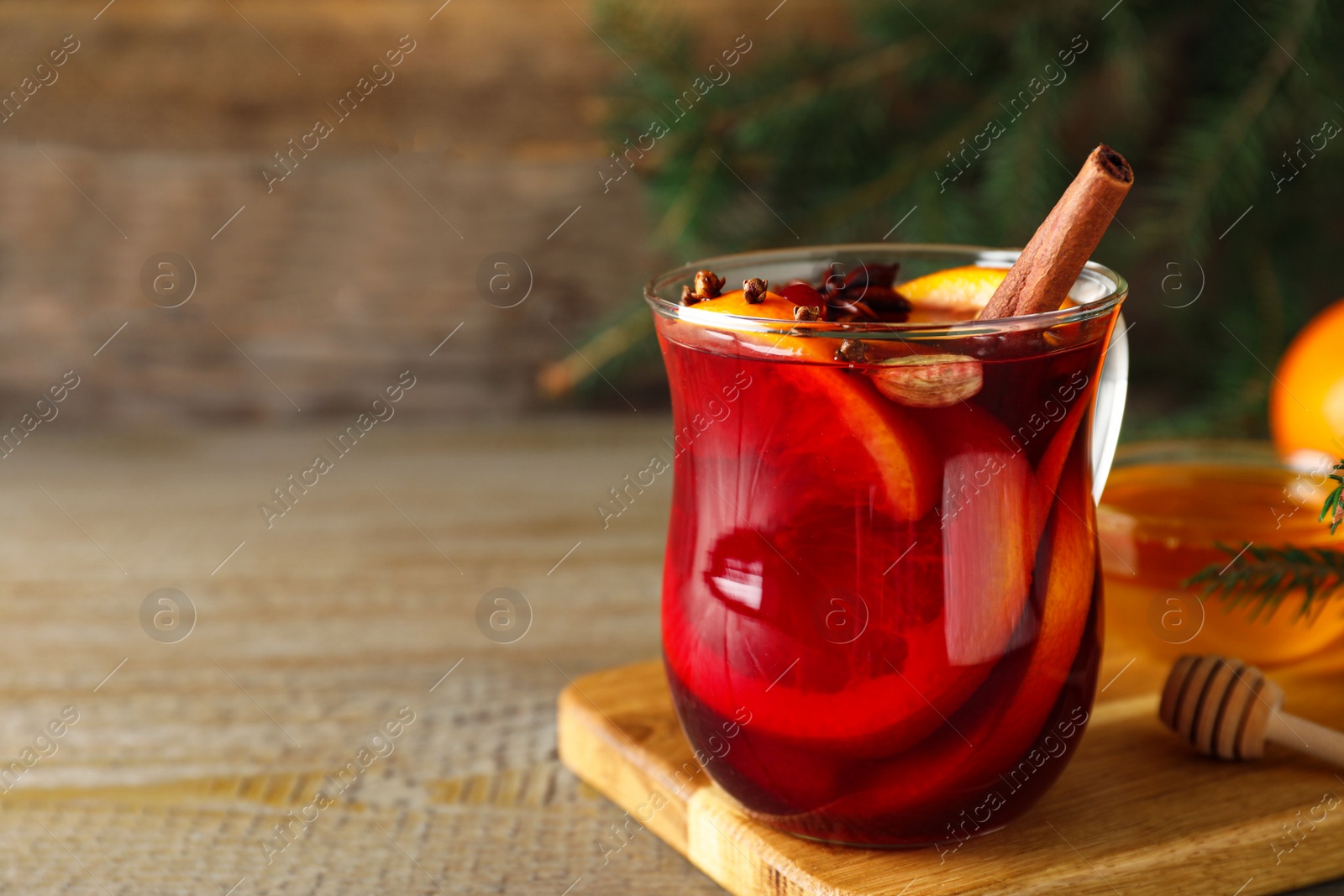 Photo of Glass cup of tasty mulled wine on wooden table. Space for text