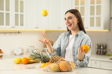 String bag with fresh fruits on light marble table. Woman throwing lemon in kitchen