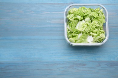 Glass container with fresh cabbage on light blue wooden table, top view. Space for text