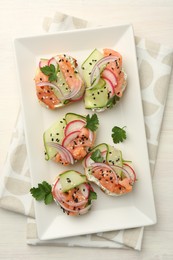 Tasty canapes with salmon served on white wooden table, top view