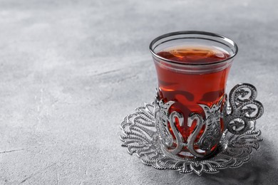 Photo of Glass of traditional Turkish tea in vintage holder on light grey table, closeup. Space for text