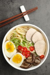 Photo of Delicious ramen with meat in bowl and chopsticks on grey textured table, top view. Noodle soup