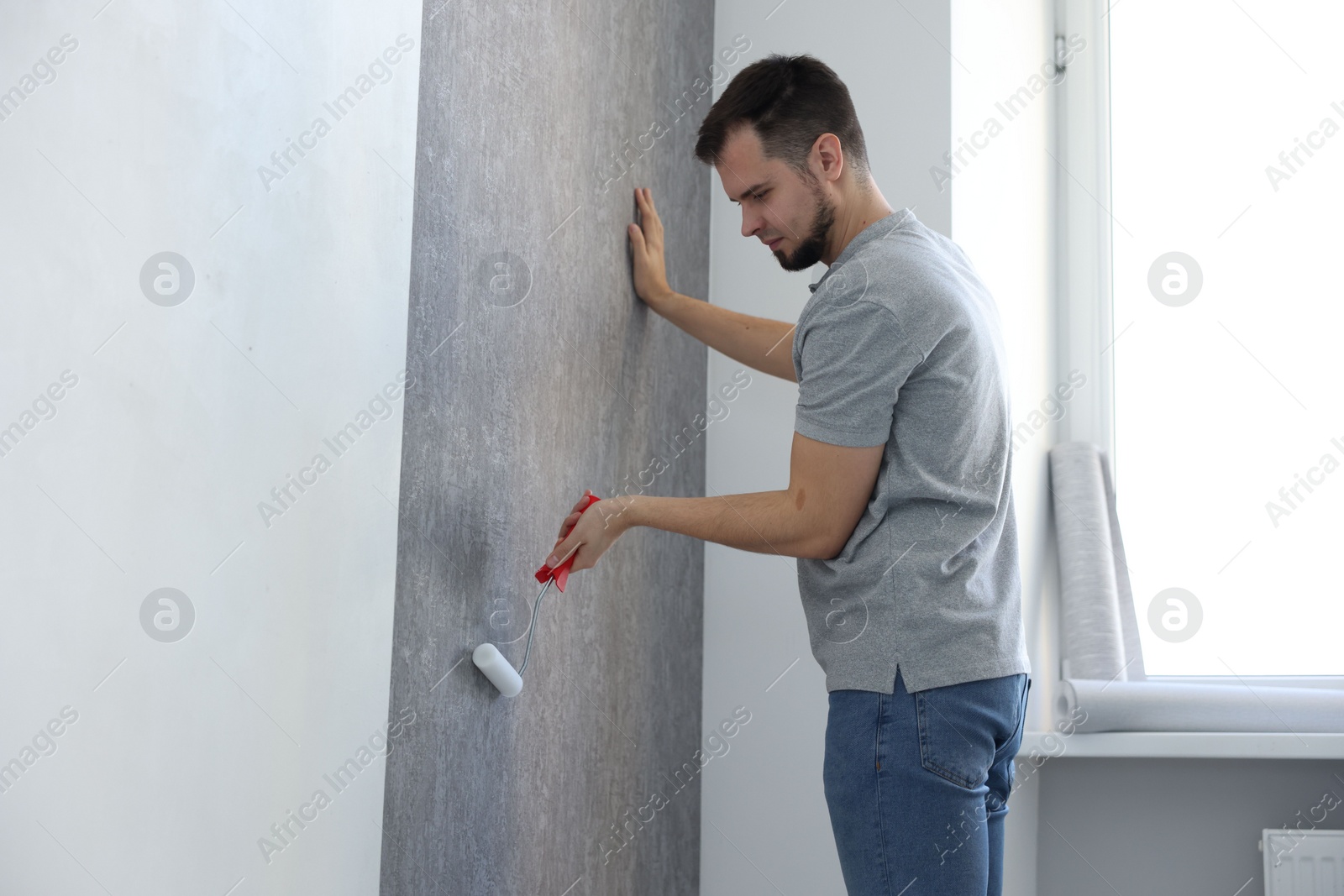 Photo of Man hanging stylish gray wallpaper in room