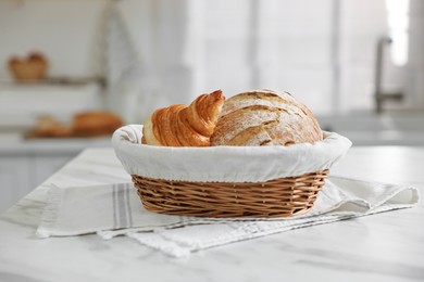 Photo of Wicker bread basket with freshly baked loaf and croissant on white marble table in kitchen