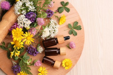 Flat lay composition with bottles of essential oil, flowers and herbs on white wooden table