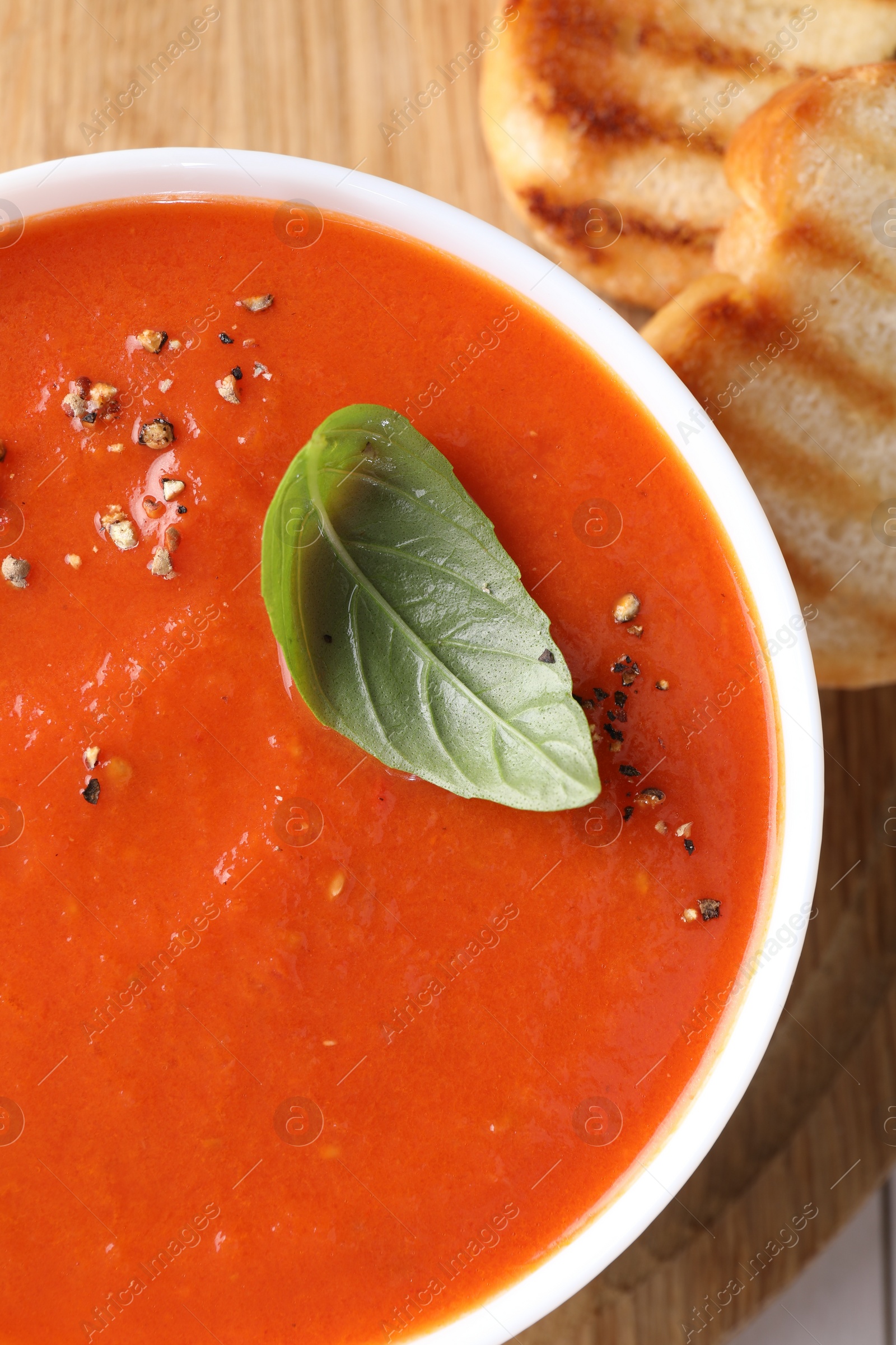 Photo of Delicious tomato soup with basil, spices and bread on table, top view