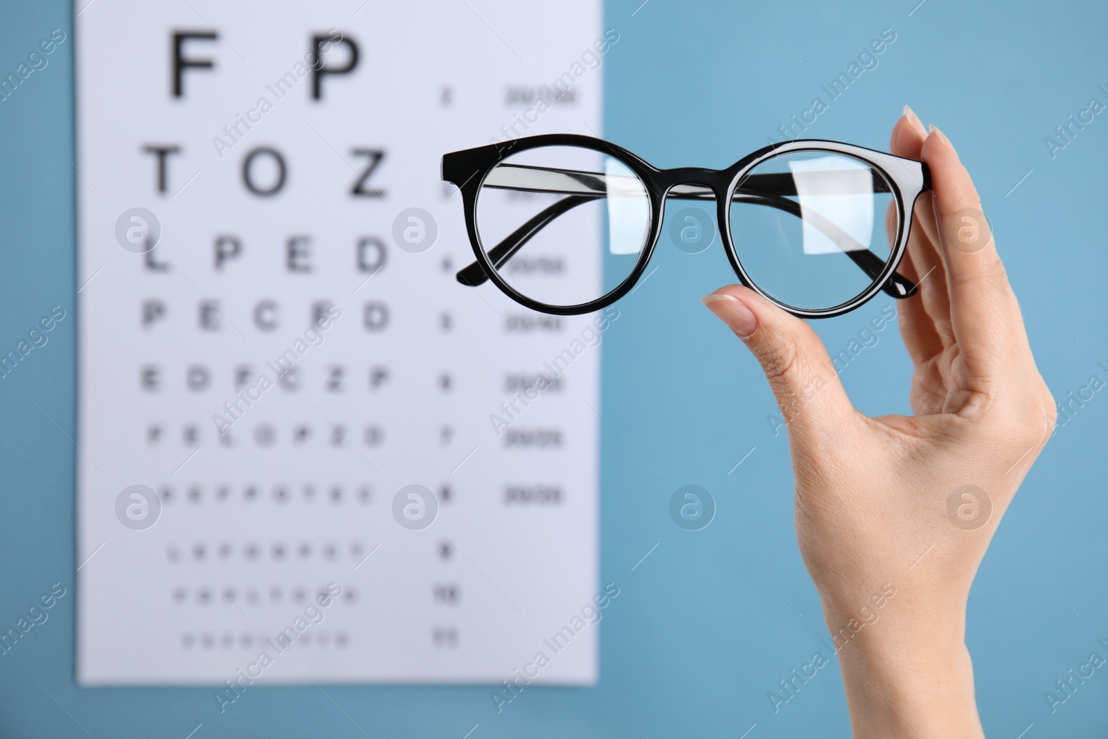 Photo of Woman holding glasses against eye chart on blue background, closeup. Ophthalmologist prescription