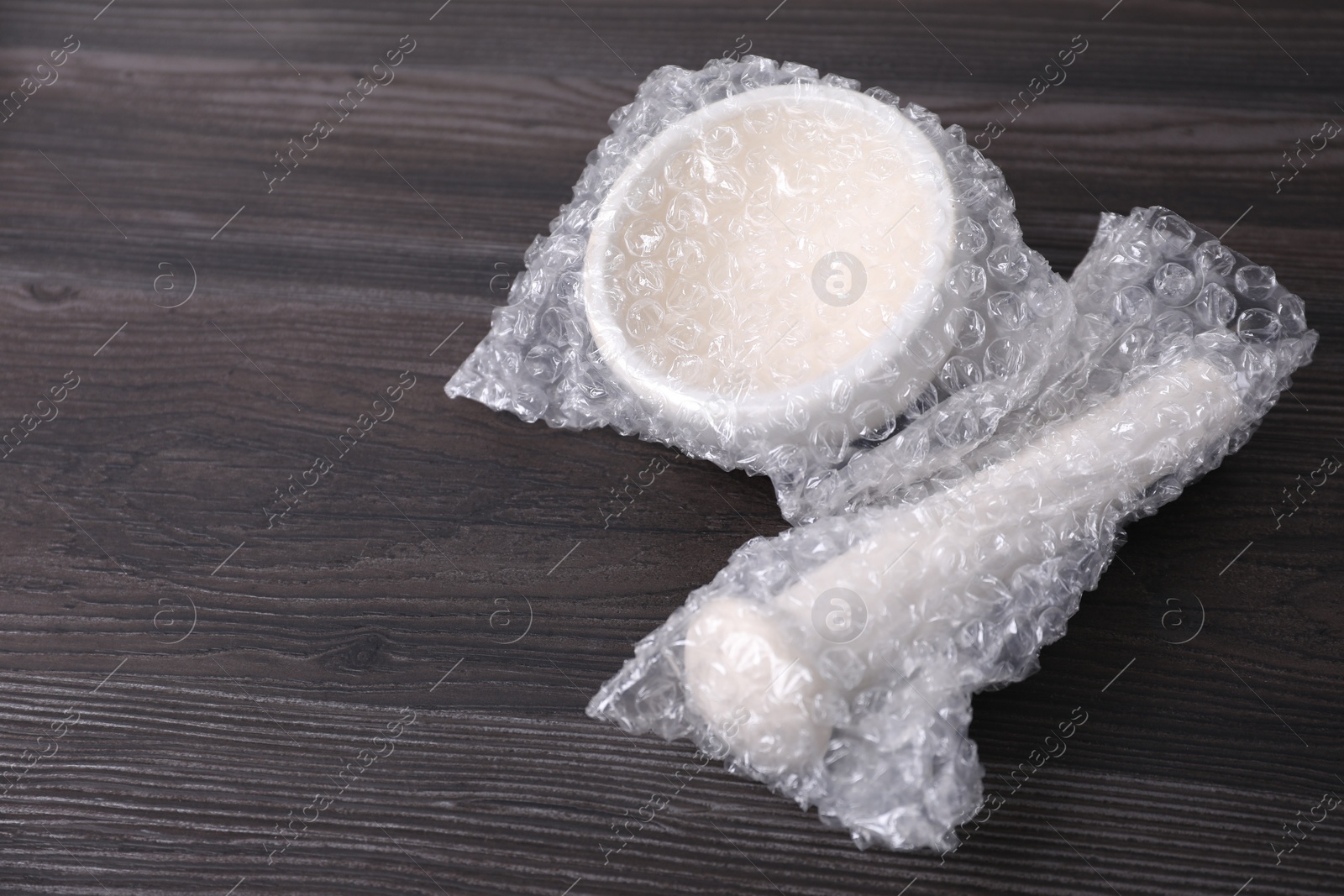 Photo of Mortar and pestle packed in bubble wrap on dark wooden table. Space for text