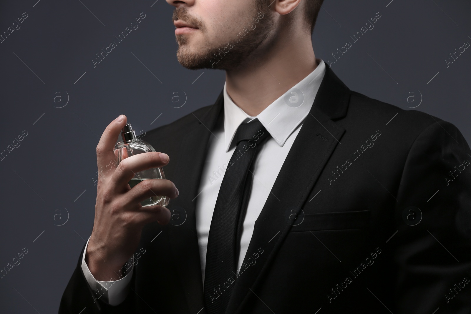 Photo of Handsome man in suit using perfume on dark background, closeup