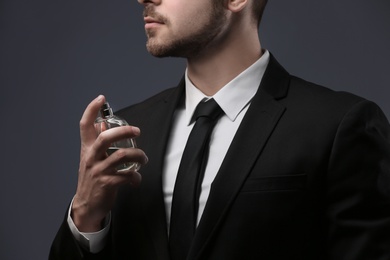 Photo of Handsome man in suit using perfume on dark background, closeup