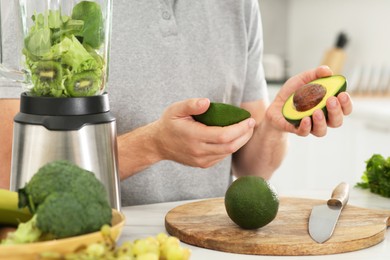 Man holding halves of avocado for delicious smoothie at white table in kitchen, closeup