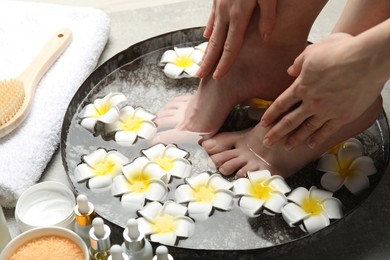 Photo of Woman soaking her feet in bowl with water and flowers on floor, closeup. Spa treatment