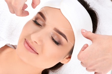 Photo of Young woman having professional eyebrow correction procedure in beauty salon