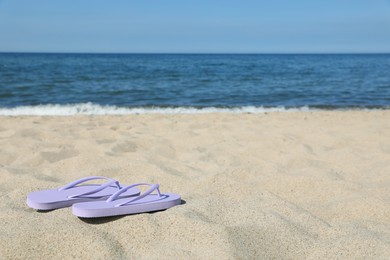 Photo of Stylish violet flip flops on beach sand, space for text