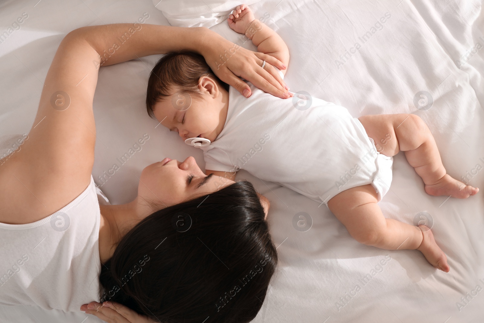 Photo of Young mother resting near her sleeping baby on bed, top view