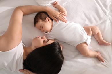 Young mother resting near her sleeping baby on bed, top view