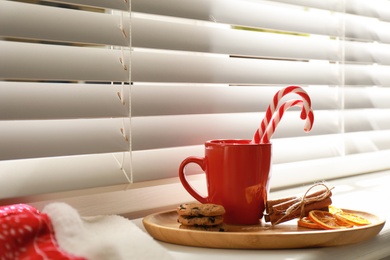 Photo of Cup of hot winter drink and treats on windowsill indoors. Space for text