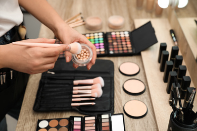 Professional makeup artist with brush and blusher at wooden table indoors, closeup