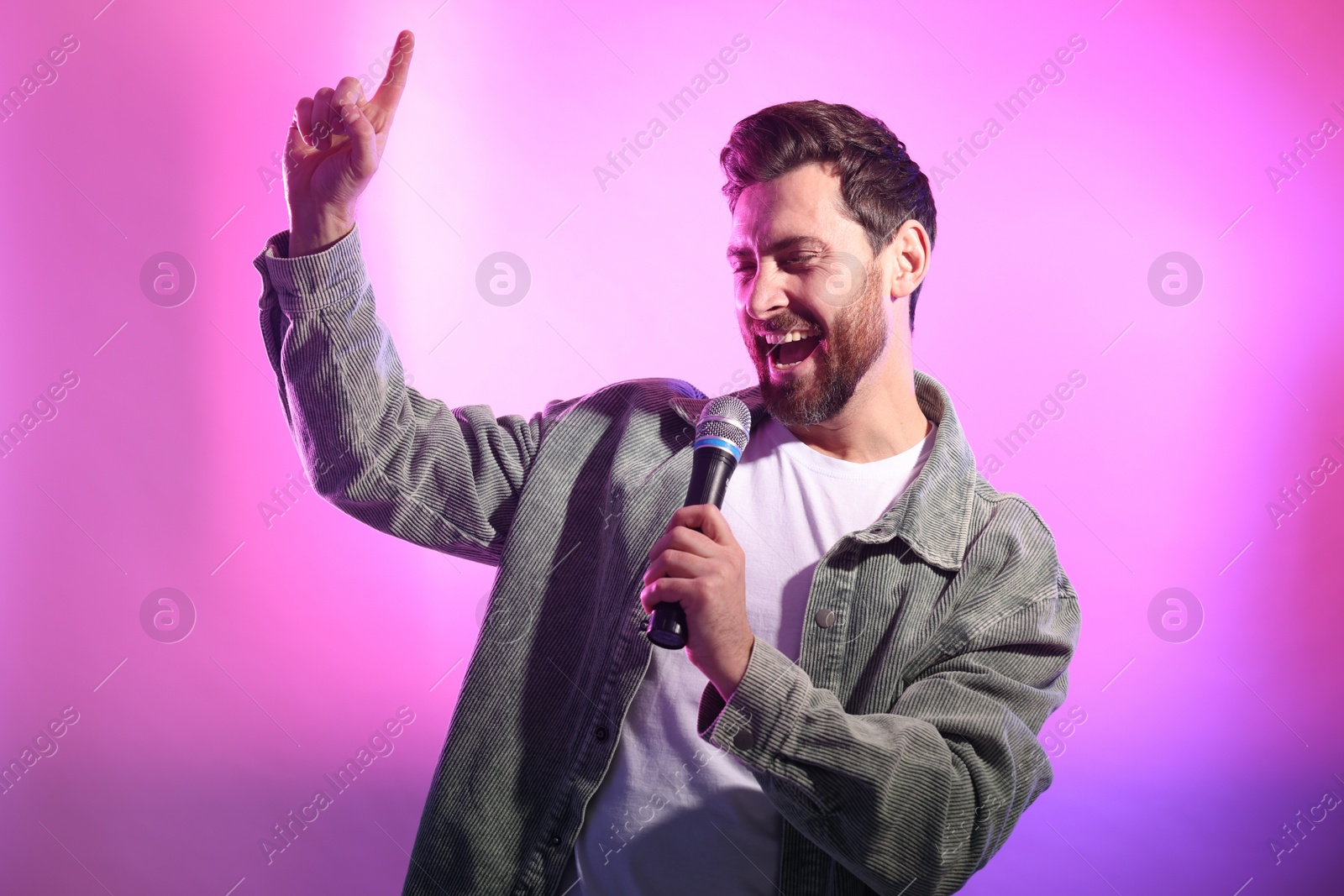 Photo of Handsome man with microphone singing on pink background