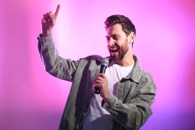 Handsome man with microphone singing on pink background