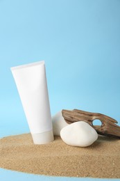 Tube of cream, stones and bark on sand against light blue background. Cosmetic product