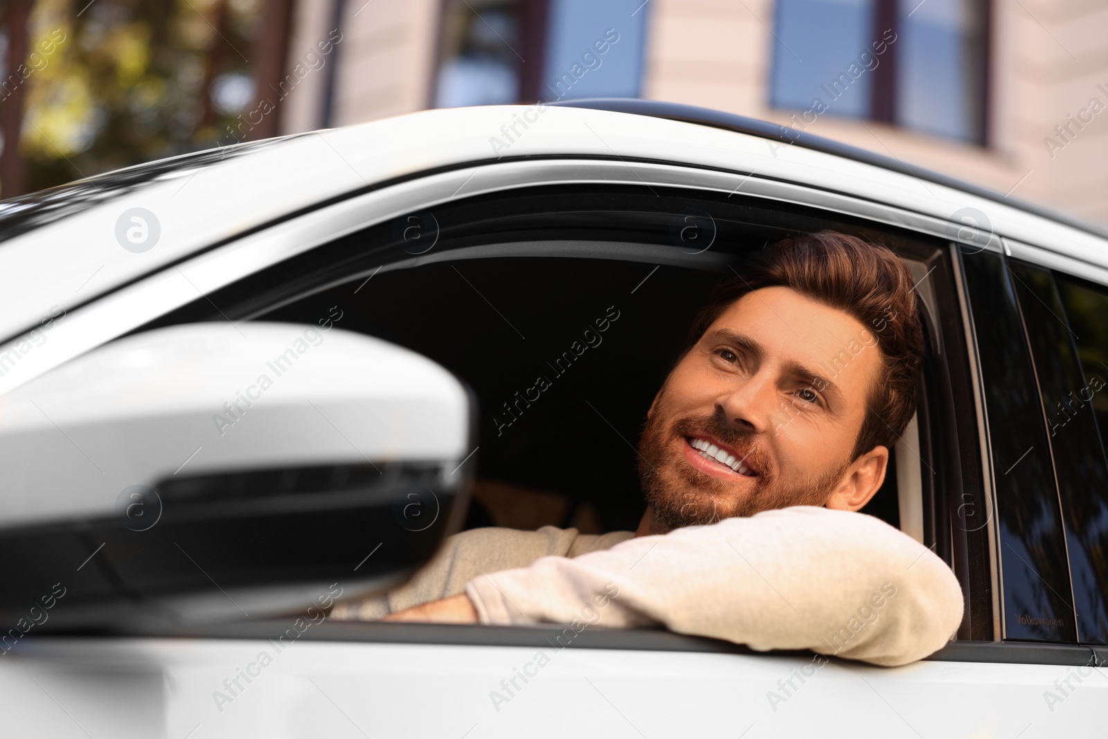 Photo of Happy man looking out of car window on city street, view from outside. Enjoying trip