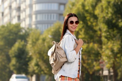 Beautiful young woman with stylish beige backpack on city street