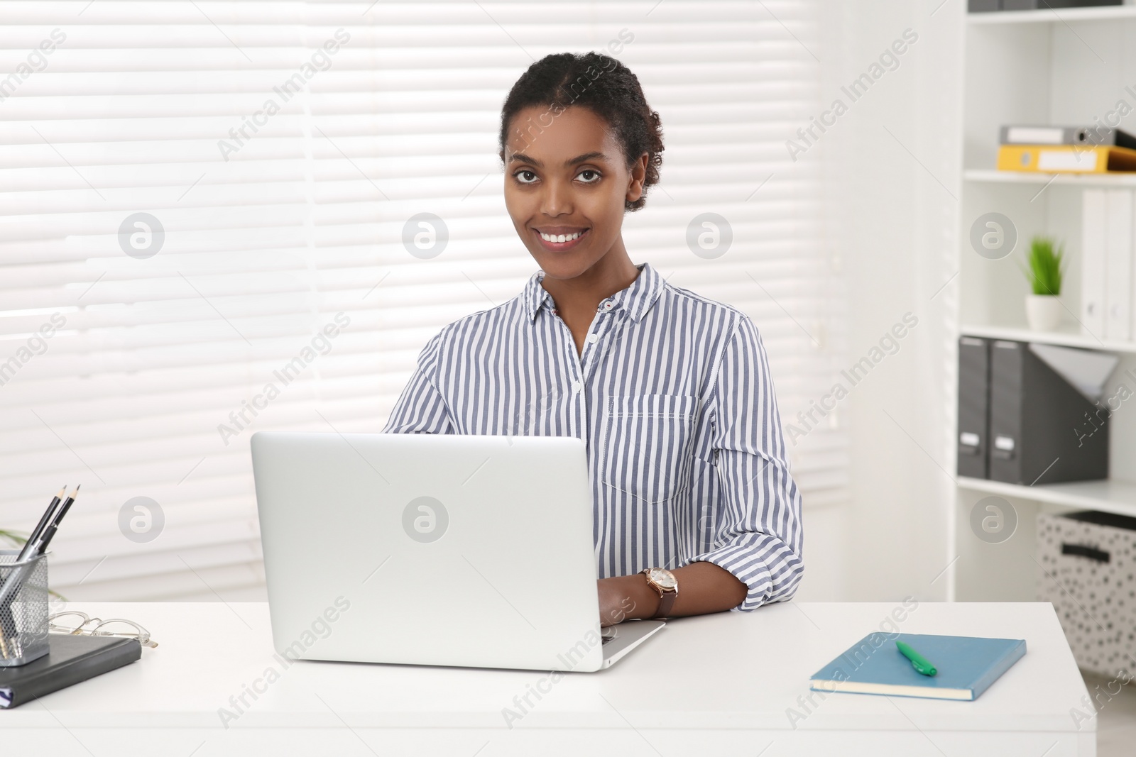 Photo of Smiling African American intern working on laptop at white table in office