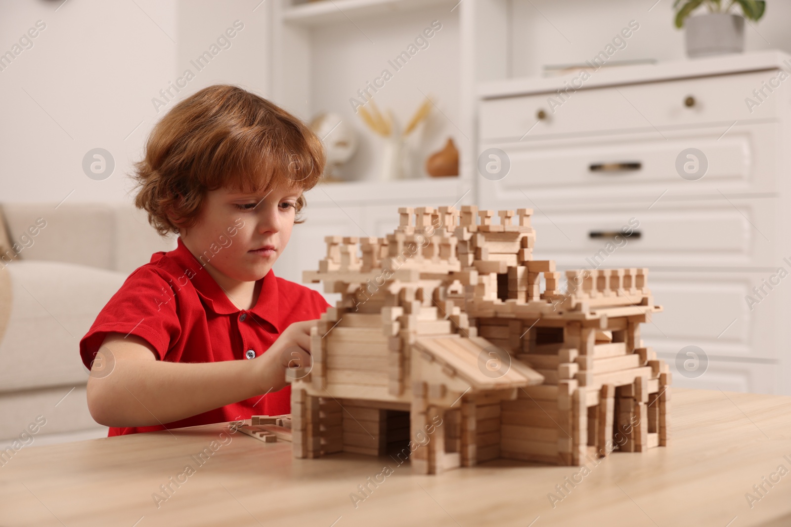 Photo of Cute little boy playing with wooden castle at table in room. Child's toy