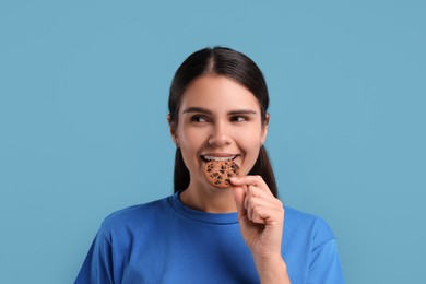 Photo of Young woman with chocolate chip cookie on light blue background