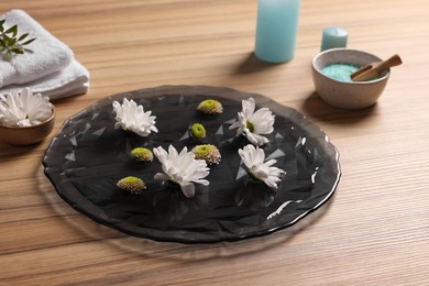 Photo of Plate with water, flowers, burning candles and sea salt on wooden floor. Pedicure procedure
