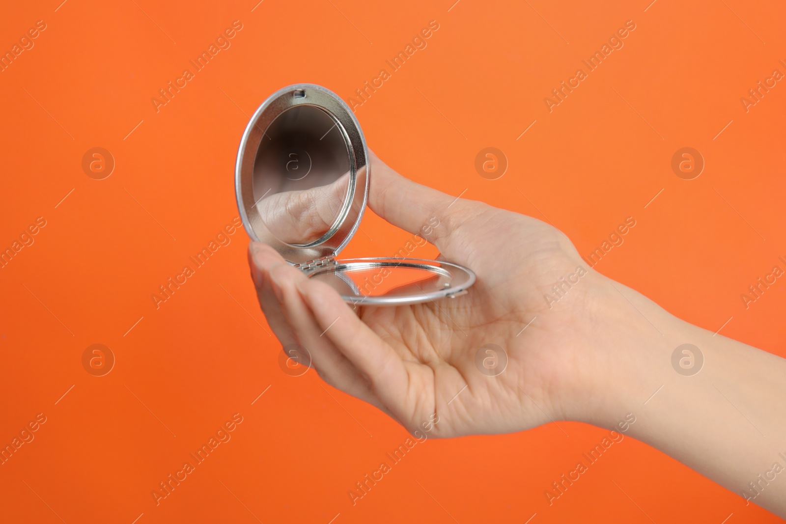 Photo of Woman holding stylish cosmetic pocket mirror on orange background, closeup