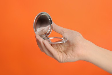 Woman holding stylish cosmetic pocket mirror on orange background, closeup