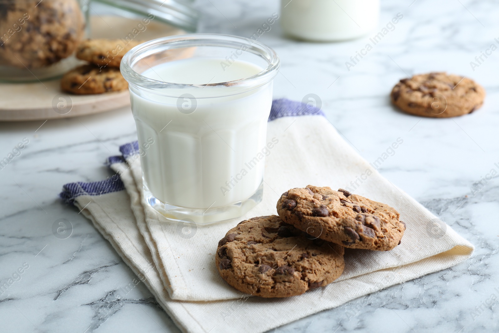 Photo of Tasty chocolate chip cookies and glass of milk on white marble table, closeup