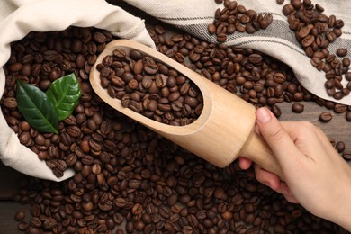 Photo of Woman taking scoop of roasted coffee beans from bag at wooden table, closeup