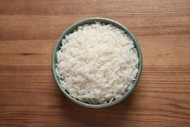Bowl of cooked rice on wooden background, top view