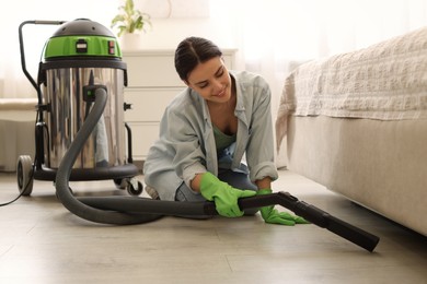 Photo of Young woman vacuuming floor near bed indoors
