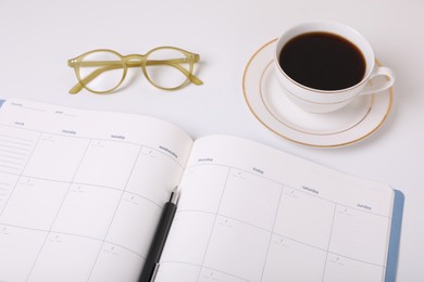 Open monthly planner, coffee, glasses and pen on white background