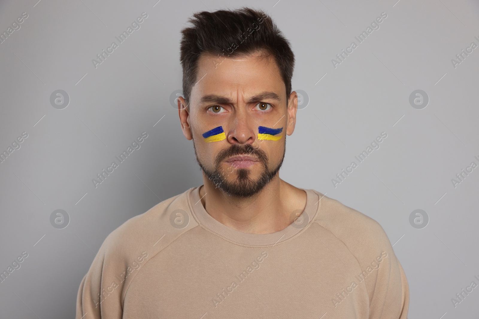 Photo of Angry man with drawings of Ukrainian flag on face against light grey background