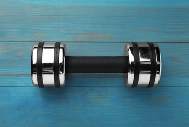 One dumbbell on light blue wooden table, top view
