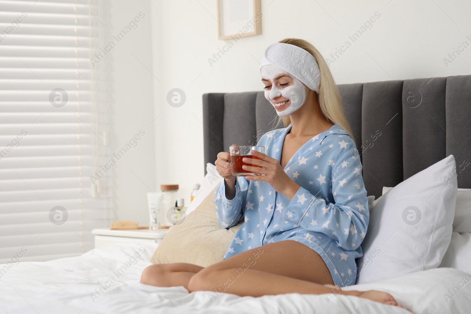 Photo of Young woman with face mask drinking tea on bed at home, space for text. Spa treatments