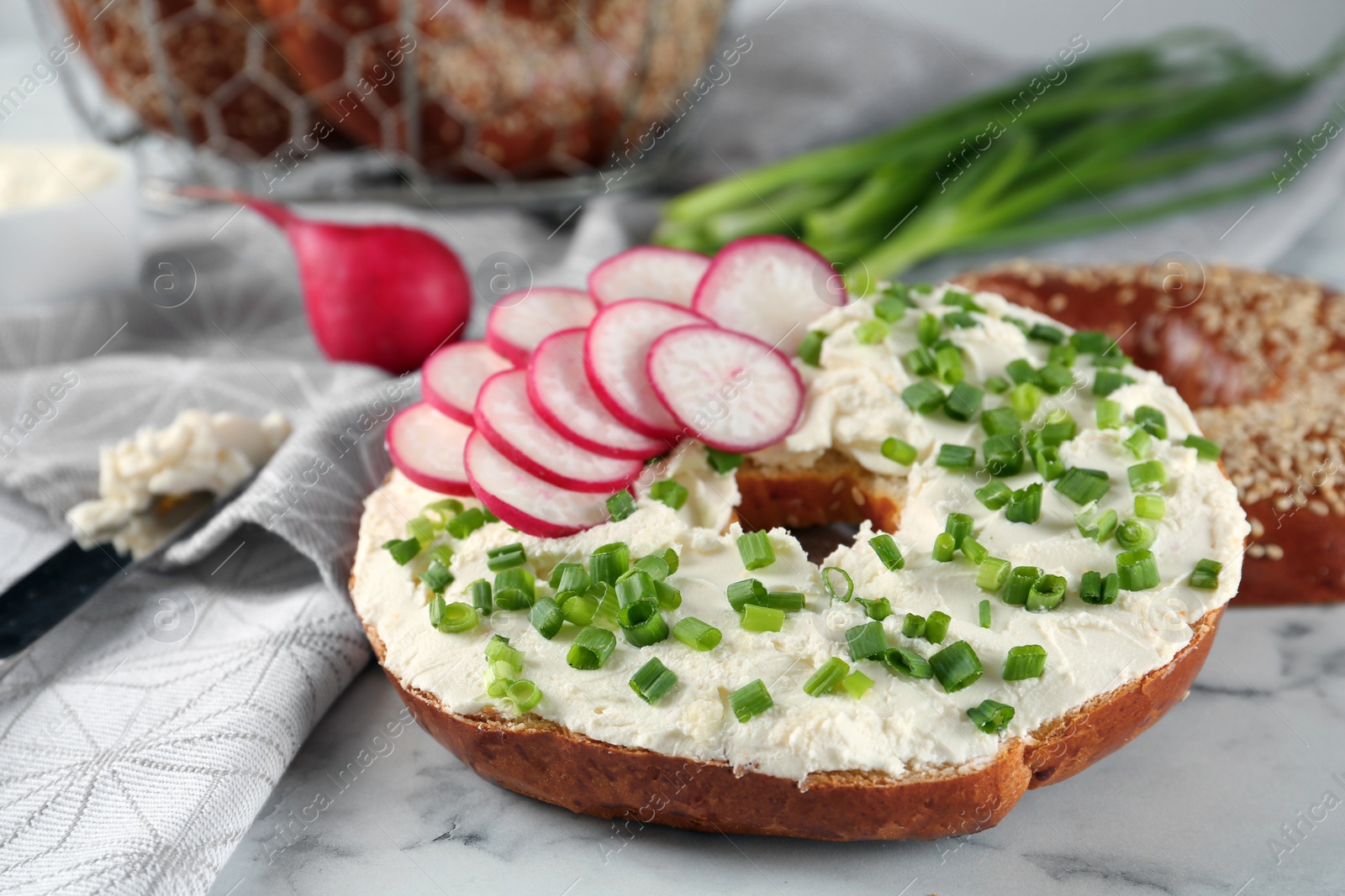 Photo of Delicious bagel with cream cheese, radish and green onion on white marble table, closeup