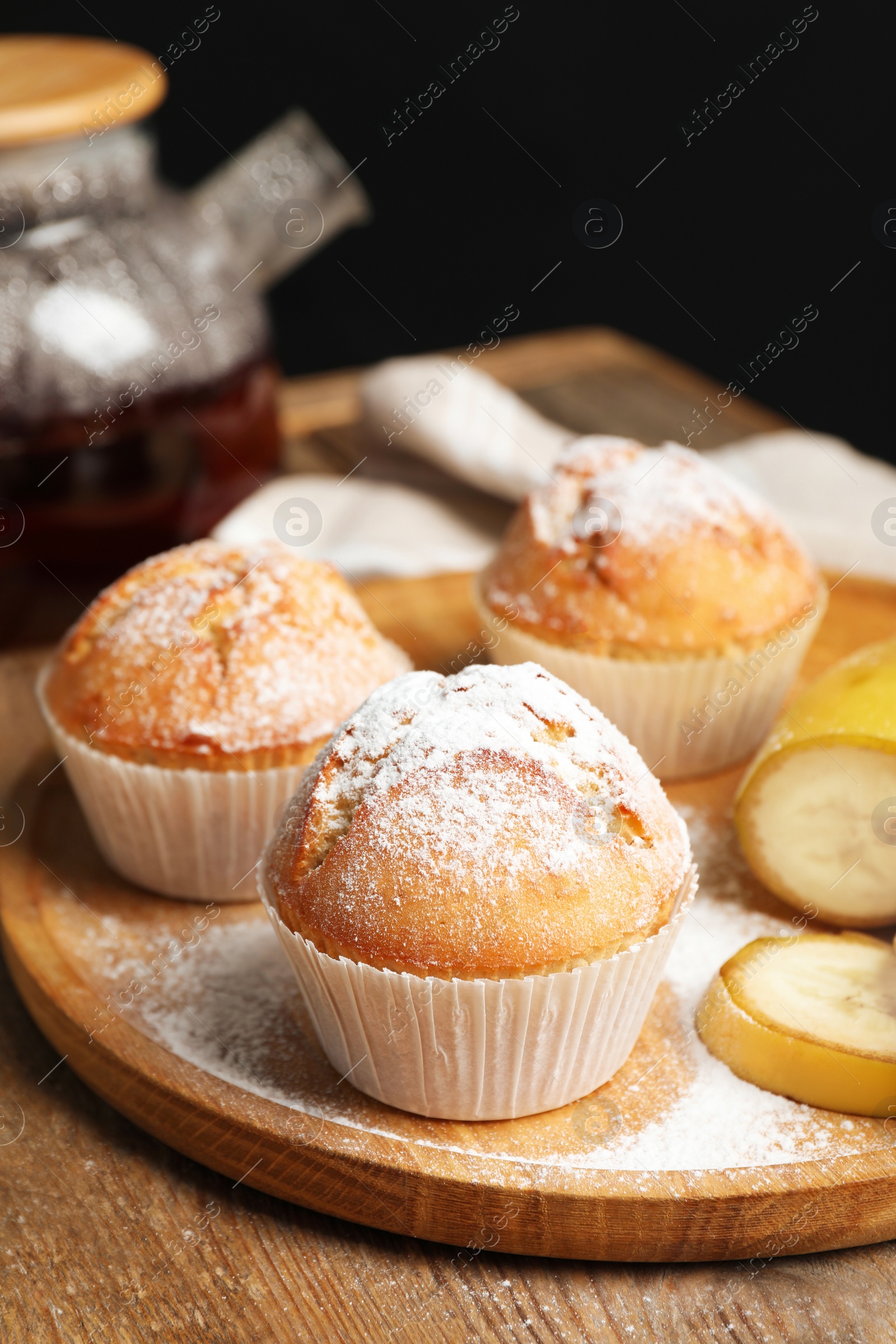 Photo of Tasty muffins served with banana slices on wooden table against dark background