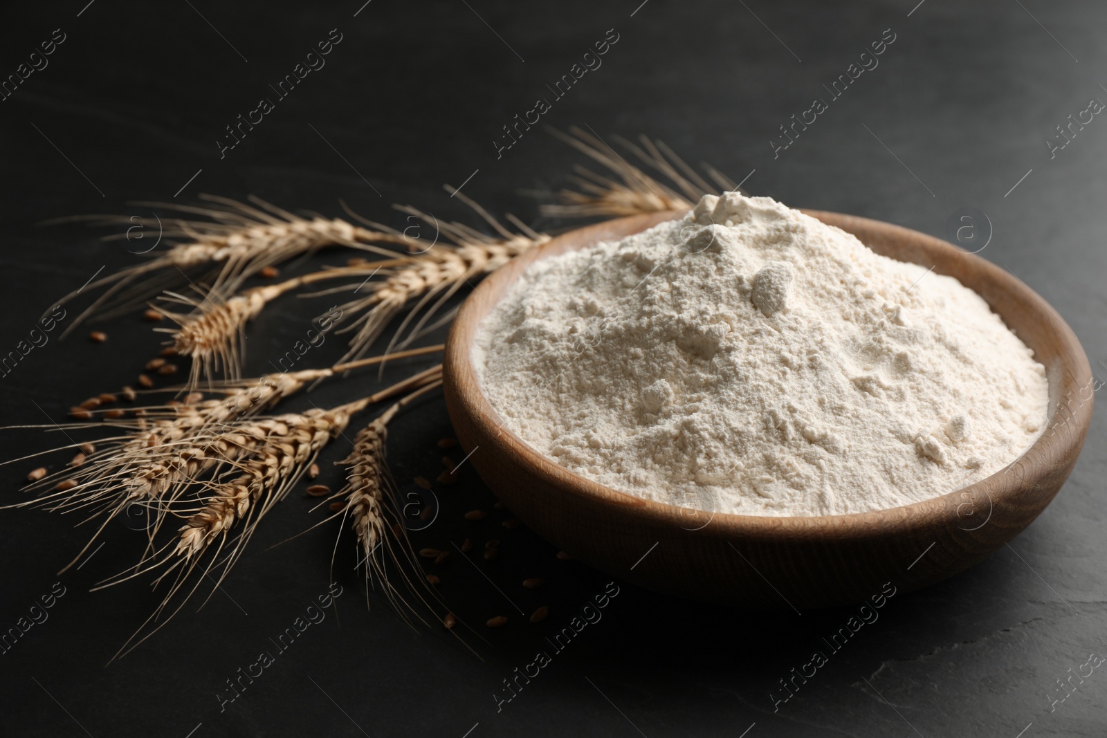 Photo of Wooden plate with flour and wheat ears on black table