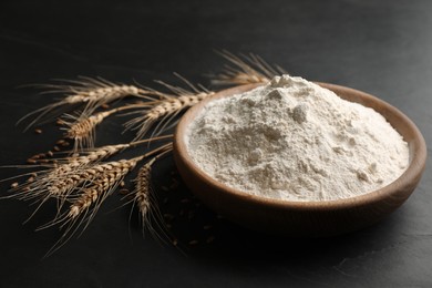 Photo of Wooden plate with flour and wheat ears on black table