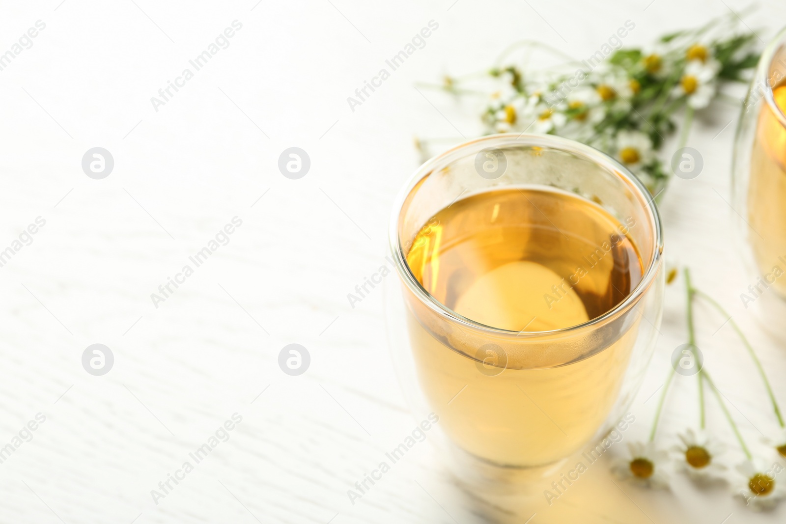 Photo of Delicious chamomile tea in glass on white table. Space for text